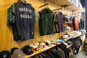A retail clothing display with multiple apparel items hanging on wooden shelves all of which are available on the Rockets and Rascals online store.